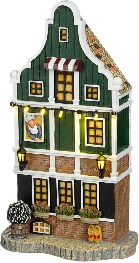 Groen Zaanse huisje met kerstverlichting, met een schilderij van een persoon in een raam en bloempotten.