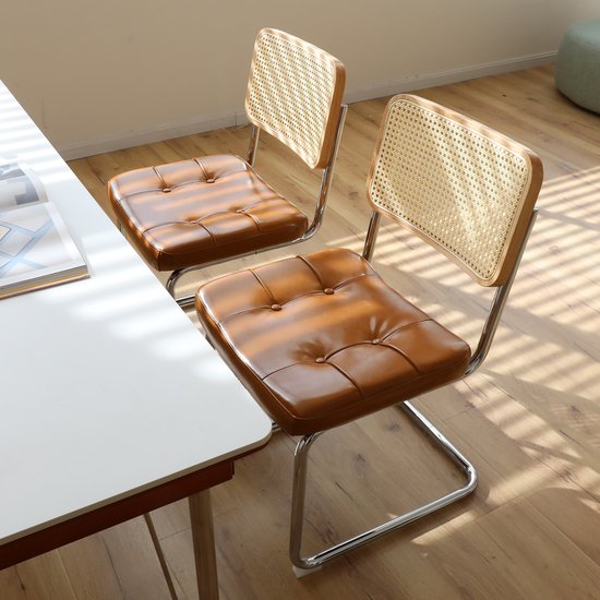 Twee bruine eetkamerstoelen met kunstleren zitting en rotan rugleuning, gefotografeerd in een kamer.