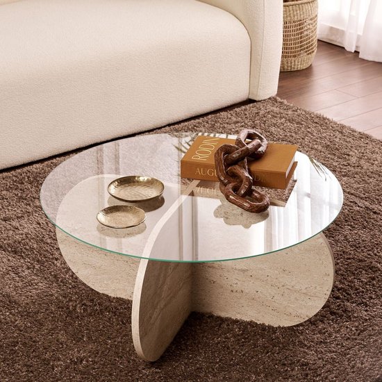 Salontafel met rond glazen blad en beige travertin onderstel, met gouden schaaltjes en boek.