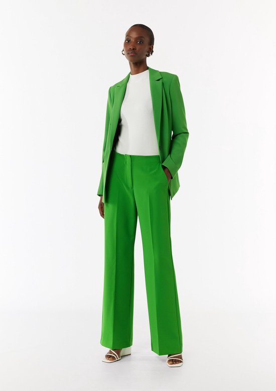 Model in een felgroene pantalon, witte top en bijpassende blazer.