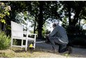 Man op knieën gebruikt de gele voegenborstel bij een witte tuinbank.