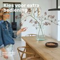Vrouw met blonde haren, blauwe spijkerjas, houdt witte afstandsbediening vast. "Kies voor extra bediening."