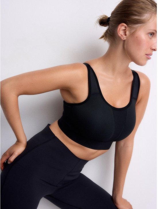 Zijaanzicht van een model in zwarte sportbeha en legging, benadrukt de pasvorm.