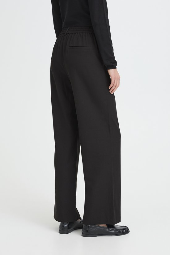 Een vrouw draagt een zwarte wijde broek, gezien vanaf de achterkant.