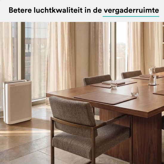 Witte luchtreiniger in een vergaderruimte met grote tafel en stoelen.