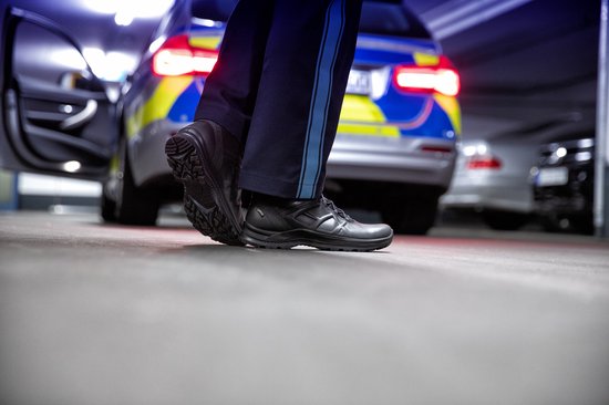 Blauwe politiebroek met blauwe streep, gedragen met zwarte schoenen met profielzool.