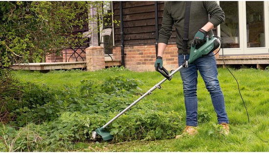 Man maait hoog gras met een Bosch grastrimmer in een tuin.
