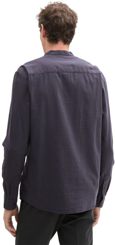 Man met rug naar de camera, draagt donkerblauw overhemd met opstaande kraag.