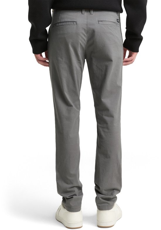 Achterkant van grijze chino broek met witte sneakers.