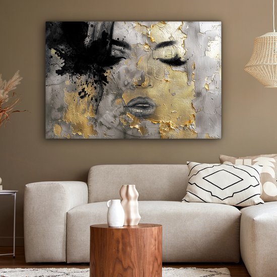 Abstract schilderij van een gezicht met zwarte verfspatten en gouden accenten, boven een bank in een woonkamer.