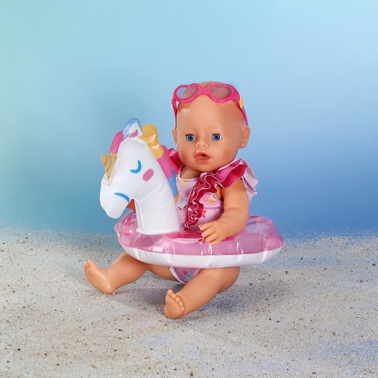 Zittende baby pop met hartjes zonnebril, glitter zwemband met eenhoorn en een glitter zwempak.