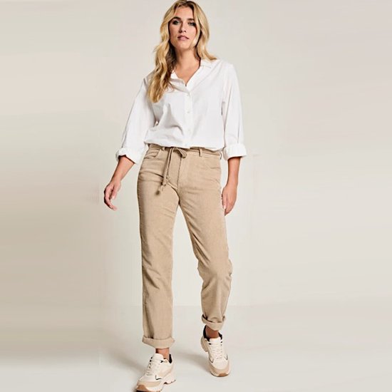 Model draagt een beige corduroy broek met trekkoord en omgeslagen pijpen, gecombineerd met een witte blouse.
