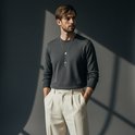 Man met donkergrijs trui en lichtbeige broek draagt een zilverkleurige rozenkrans ketting.