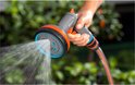 Grijze GARDENA spuit met oranje accenten sproeit water.