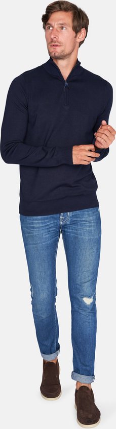 Man met donkerblauwe trui met rits tot de borst, jeans en bruine schoenen.