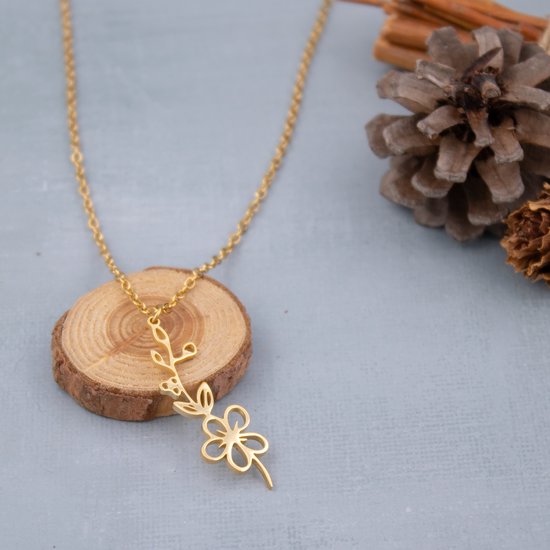 Gouden ketting met een delicate bloem- en takjeshanger, gepresenteerd op een houten schijf.