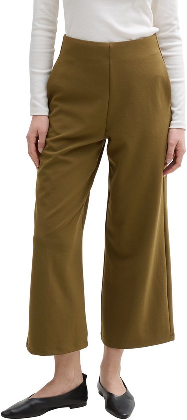 Model draagt een olijfgroene culotte met wijde pijpen en een hoge taille. Ze draagt een witte top met lange mouwen.