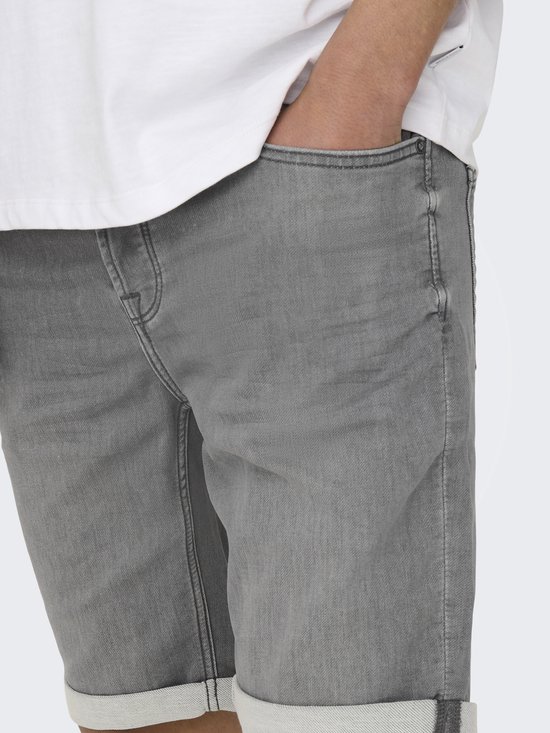 Close-up van een grijze denimshort met omgeslagen broekspijpen. Een hand zit in de zak.