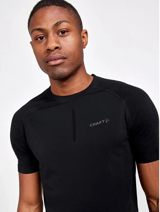 Close-up van een man in zwart Craft sportshirt met korte mouwen. Gestructureerde stof op de schouders en mouwen.