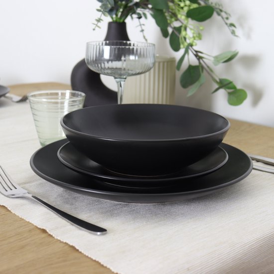 Een tafel gedekt met matzwarte borden, met een kom erop, en bestek ernaast.