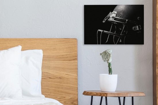 Un casque de football américain noir avec masque, sur un mur au-dessus d'une table de chevet à côté d'un lit.
