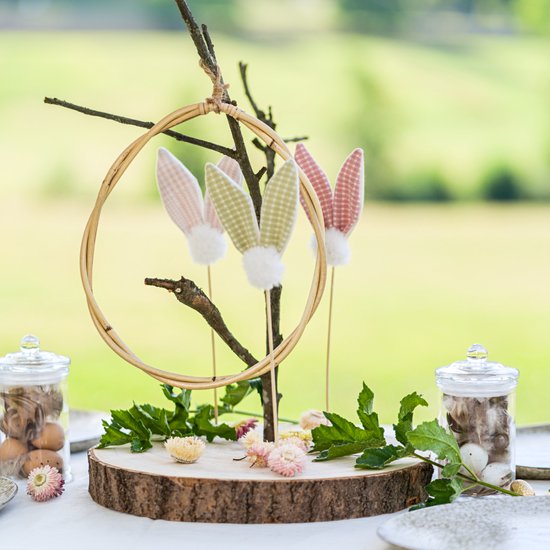 Houten decoratie met konijnenoren in pastelkleuren aan een tak met krans.