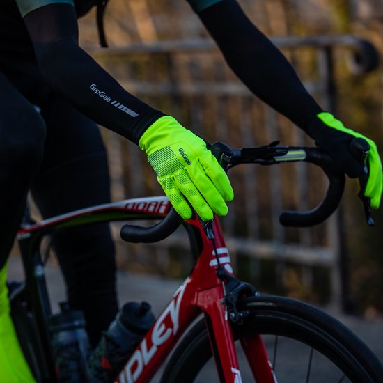 Een fietser in de herfstzon draagt een zwarte jas met hi-vis gele handschoenen en handwarmers.