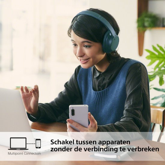 Een vrouw met een blauwe Sony WH-CH720N koptelefoon, werkend aan een laptop en telefoon.