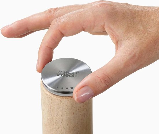 Een hand met nette nagels plaatst de RVS dop met Joseph Joseph logo op een houten pepermolen.