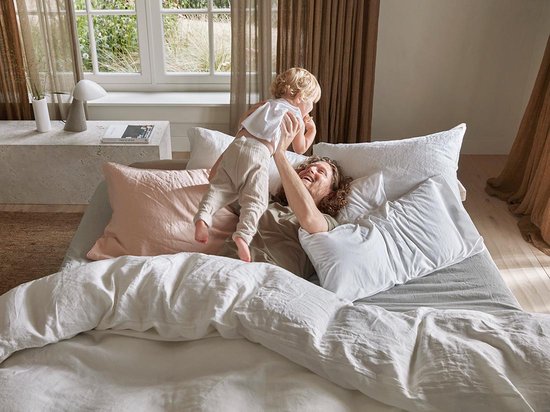 Een man met een kind op een bed met wit linnen beddengoed.
