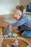 Jongen met blond haar speelt met een houten trein. Hij duwt de trein door de mijn entree.