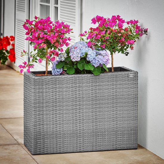 Grijze vlechtwerk plantenbak met roze en blauwe bloemen, 83x30,5x60cm.