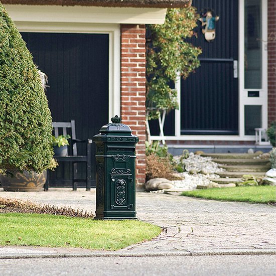 Groene, vrijstaande brievenbus met sierlijk, klassiek design bij een woning met rieten dak.