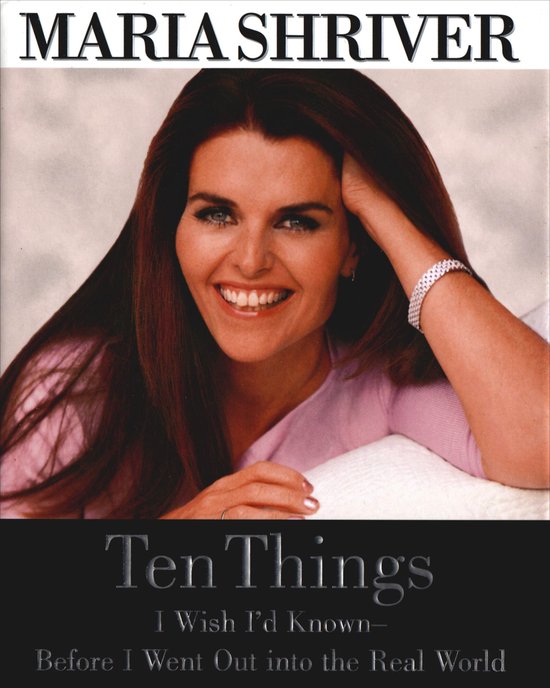 Maria Shriver lacht naar de camera, haar hand rust op haar hoofd. Ze draagt een roze trui.