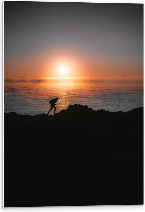 WallClassics - PVC Schuimplaat- Man lopend over Berg aan de Zee met Zonsondergang - 40x60 cm Foto op PVC Schuimplaat