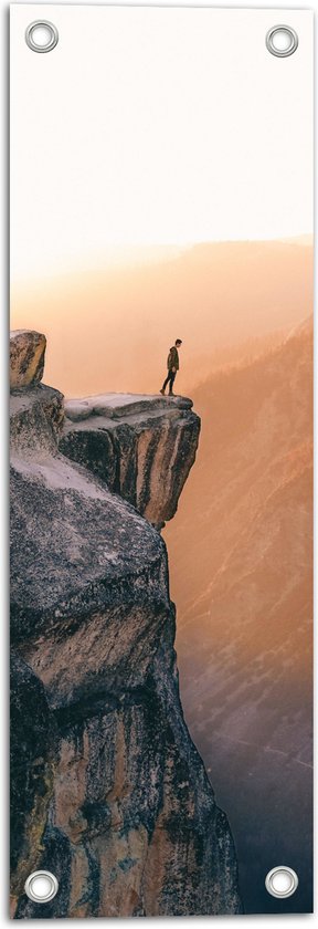 WallClassics - Tuinposter – Man aan de Rand van Hoge Cliff met Zonlicht - 20x60 cm Foto op Tuinposter (wanddecoratie voor buiten en binnen)