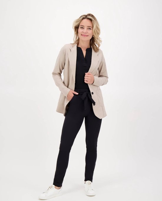 Model met zwarte broek met strikceintuur en beige gestreept jasje.