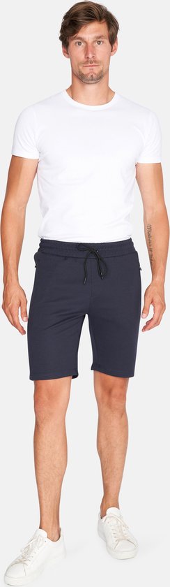 Man met witte t-shirt en donkerblauwe korte broek met trekkoord en ritssluitingen aan de zijkant.
