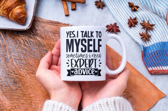 Witte mok met tekst "YES, I TALK TO MYSELF SOMETIMES I NEED EXPERT ADVICE", vastgehouden in twee handen.