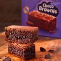 Twee Milka Choco Brownies op een houten plank met stukjes chocolade.