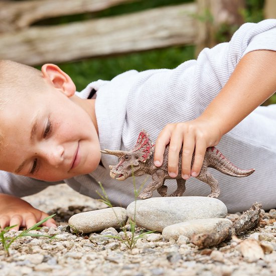 Jongen met witte hoodie kijkt naar bruine dinosaurus met rode accenten op stenen.