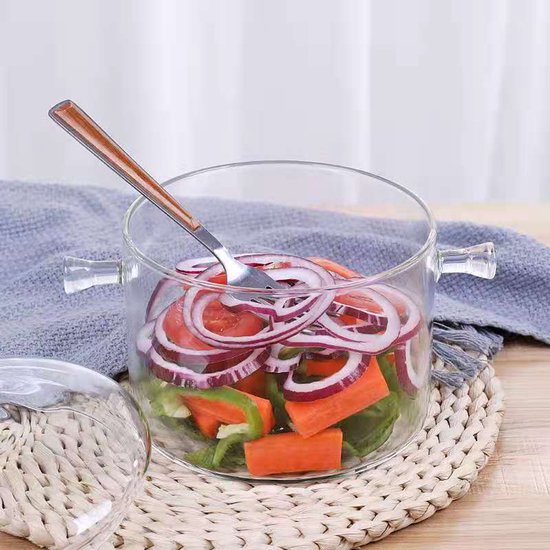 Transparante glazen pan gevuld met gesneden uienringen, wortels en paprika's op een gevlochten onderzetter.