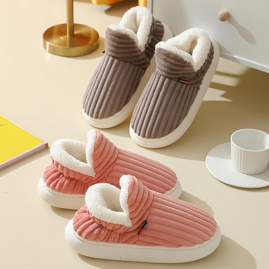Een paar roze en bruine corduroy pantoffels met witte pluche voering op een tafel.