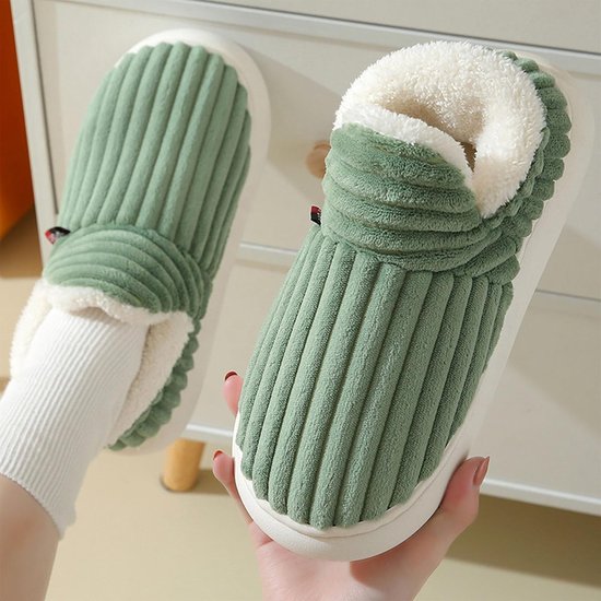 Hand die groene geribbelde pantoffels met witte voering van imitatiebont omhoog houdt.