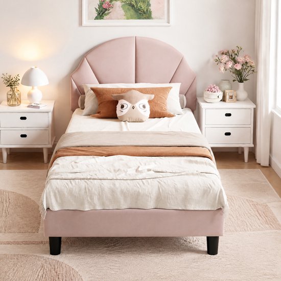 Roze gestoffeerd eenpersoonsbed met schelpvormig hoofdeinde, omringd door twee witte nachtkastjes met bloemen.