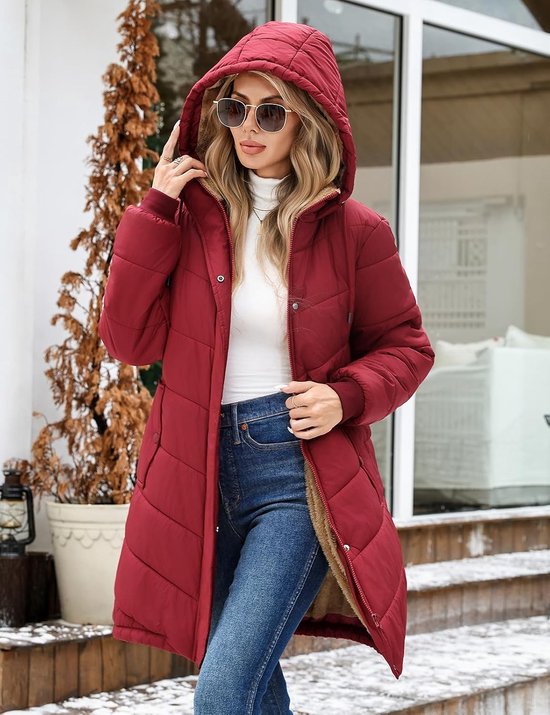 Vrouw draagt een bordeauxrode gewatteerde jas met capuchon, fleece voering, rits en zakken, staand in een wintersetting.