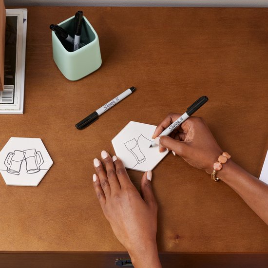 Vrouw tekent met zwarte Sharpie marker op een hexagonale tegel.