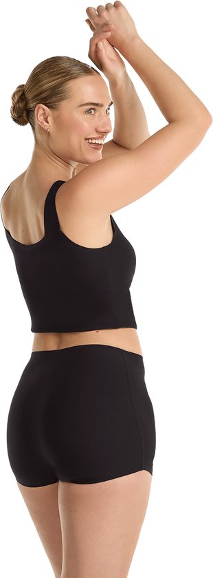 Model met blote schouders draait zich om, handen gebogen boven hoofd, draagt zwarte crop top en short.