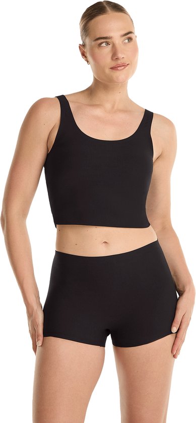 Model met blote schouders in zwarte crop top en korte broek, handen in zij.
