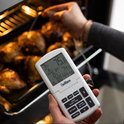 ChefAlarm kookthermometer in de hand met LCD-scherm, gebruikt bij het meten van kip in een hete oven.